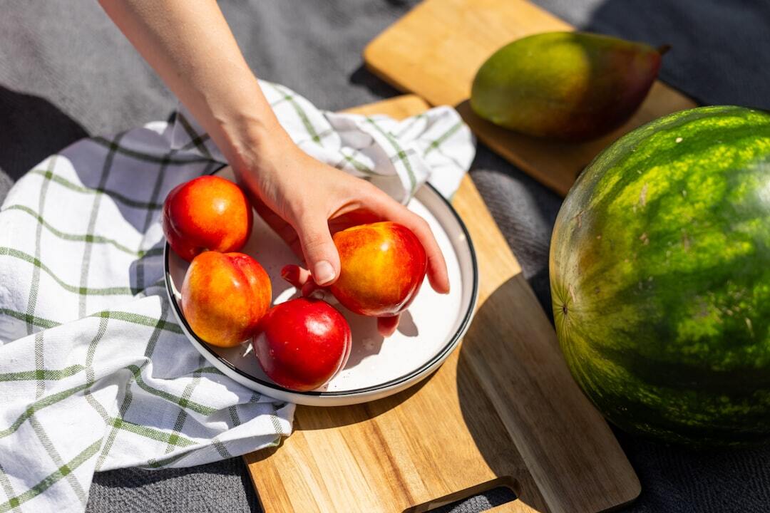 Hand picking fresh nectarines, with watermelon and mango nearby