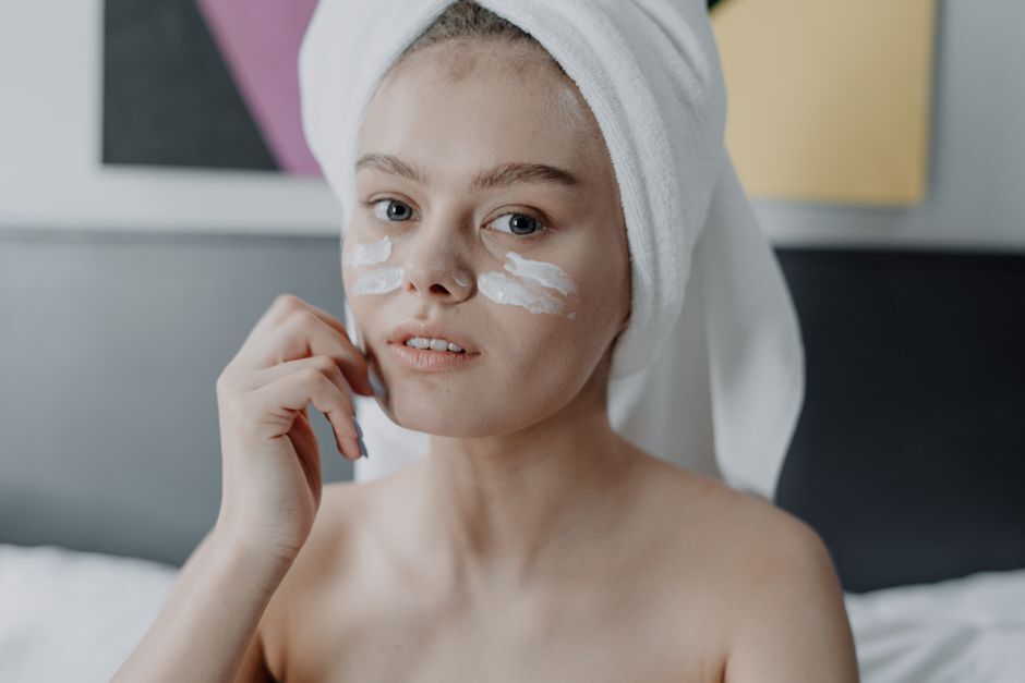 A young woman with facial cream and a towel wrapped on her head, focused on skincare