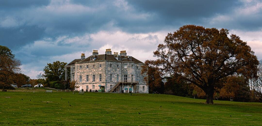 Large stone manor house with autumn tree on grassy hill