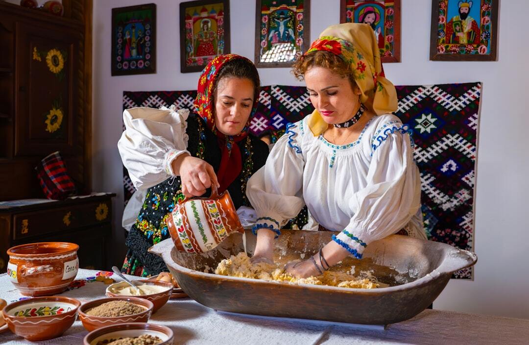 Two women in traditional folk clothing kneading dough in a large wooden bowl